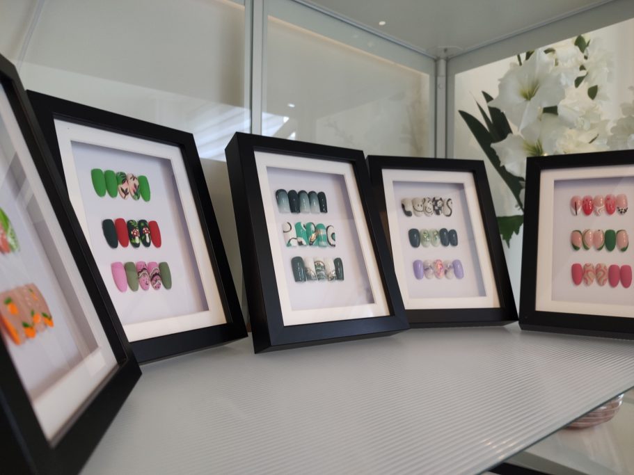 Kleurige, ingelijste nagelkunst in verschillende ontwerpen en kleuren op een vitrine.