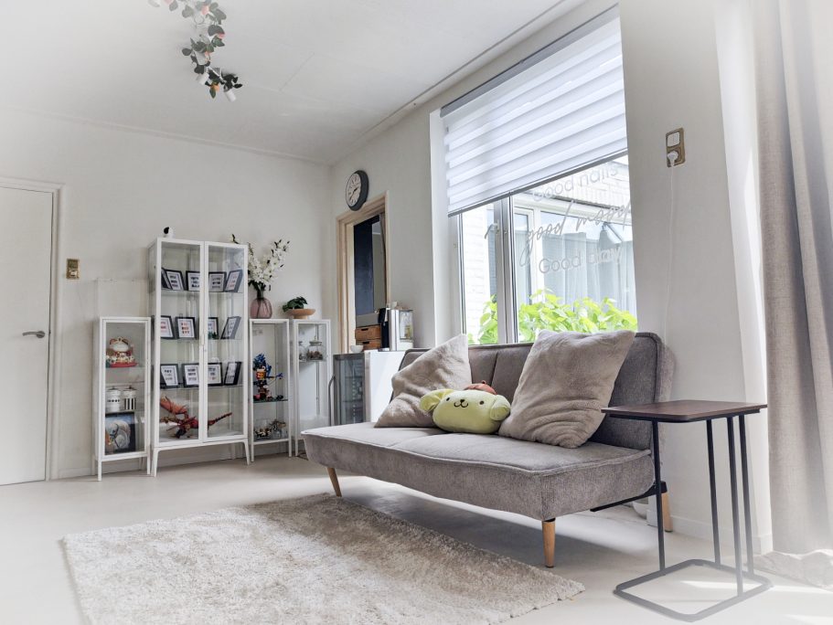 Moderne woonkamer met grijze bank, boekenkast en grote ramen.